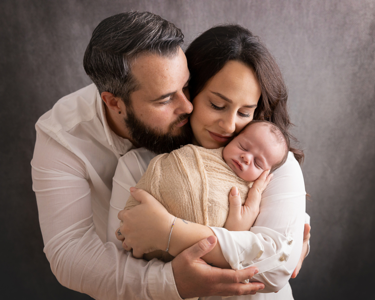 Das Familienfoto zeigt Mama und Papa mit ihrem gepuckten Neugeborenen - Neugeborenenfotografie für Stuttgart, Esslingen und Umgebung von André Weber